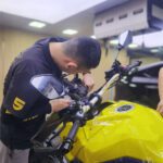 Suzuki motorcycle front fairing receiving SHIELD SPIRIT 7.5mil PCU PPF installation at direct store - detail technician squeegeeing film onto headlight area