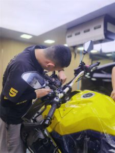 Suzuki motorcycle front fairing receiving SHIELD SPIRIT 7.5mil PCU PPF installation at direct store - detail technician squeegeeing film onto headlight area