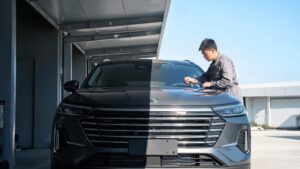 Dark SUV half under workshop canopy half in outdoor sunlight with installer examining glossy hood PPF trade-off