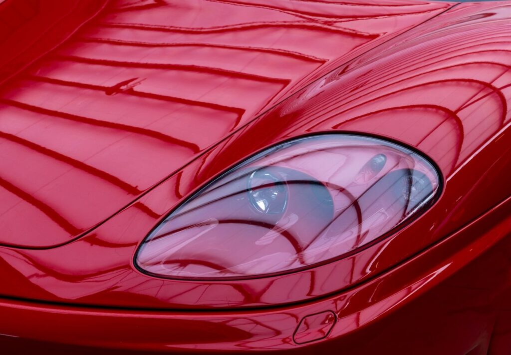 Detailed close-up of a red sports car's headlight with reflective patterns. Modern and sleek design in focus.