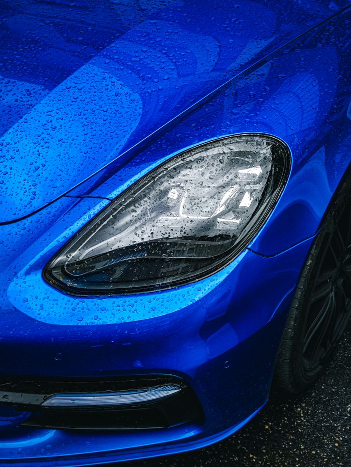 Detailed photo of a blue car's headlight covered in raindrops in Baku, Azerbaijan.