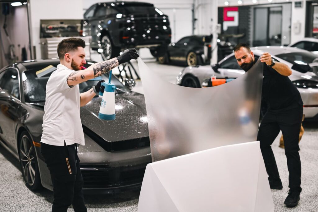 Crafting Captivating Headlines: Your awesome post title goes here Two men working in garage applying protective film on a luxury car.